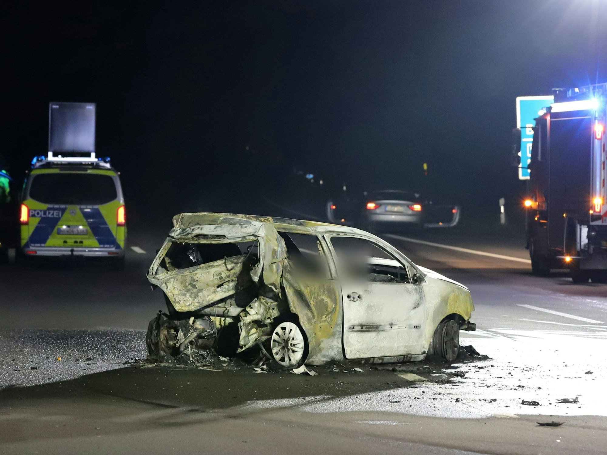 Ein völlig zerstörter und ausgebrannter Pkw steht auf einer Autobahn.