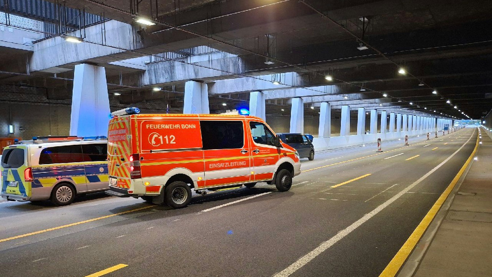 Ein Streifenwagen und ein Feuerwehrfahrzeug stehen in einem Tunnel, davor halb verdeckt ein Kleinbus.