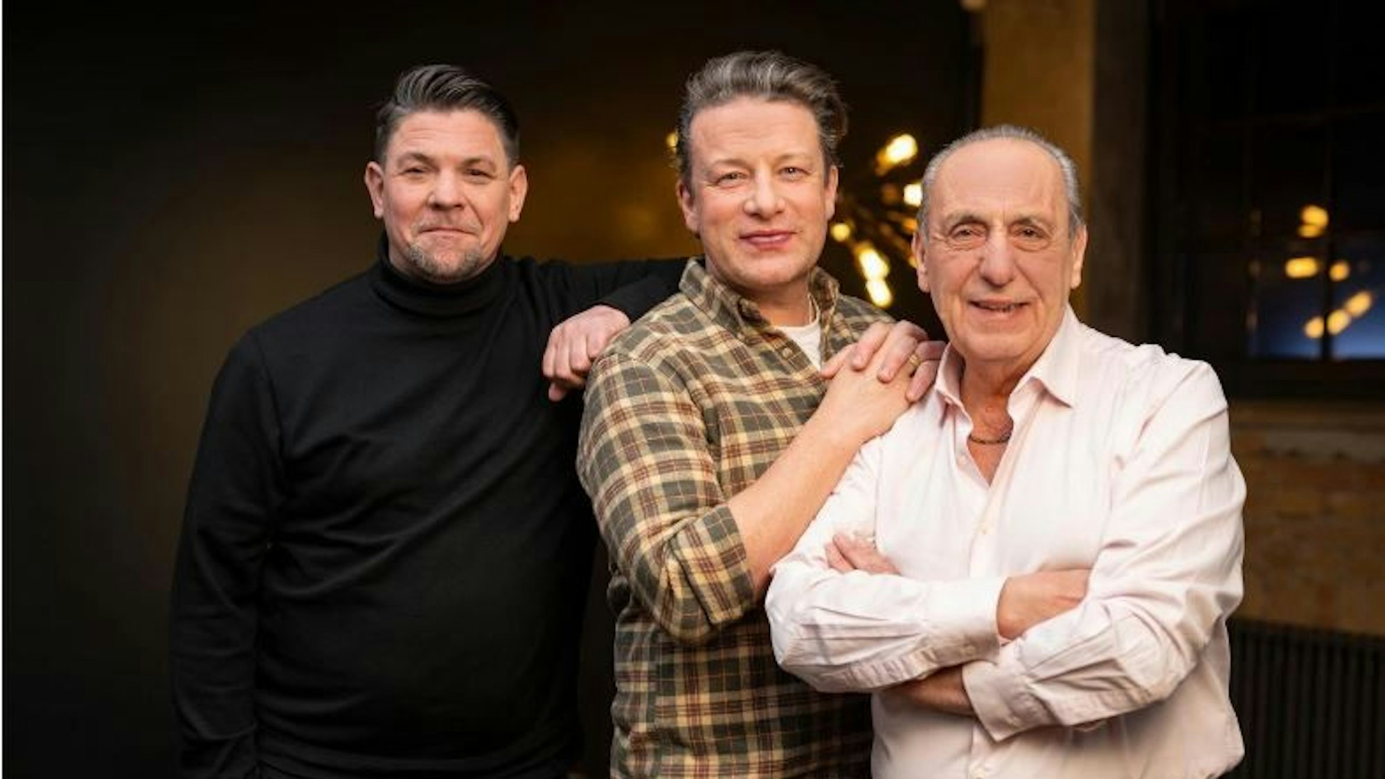 Zwei junge Männer und ein älterer Mann stehen in einer Reihe und schauen freundlich in die Kamera.