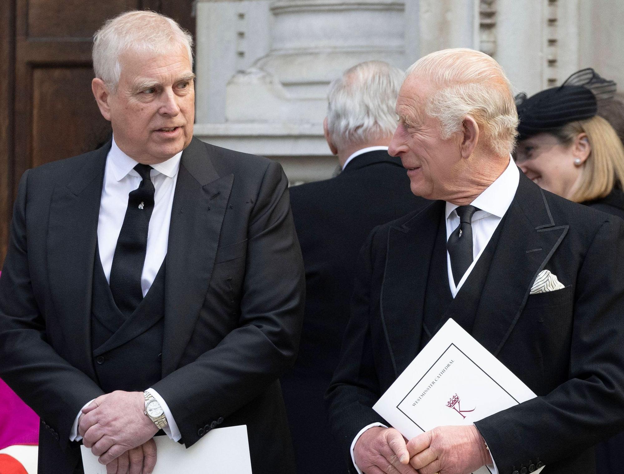 Prinz Andrew und König Charles III unterhalten sich in schwarzen Anzügen und halten Dokumente.