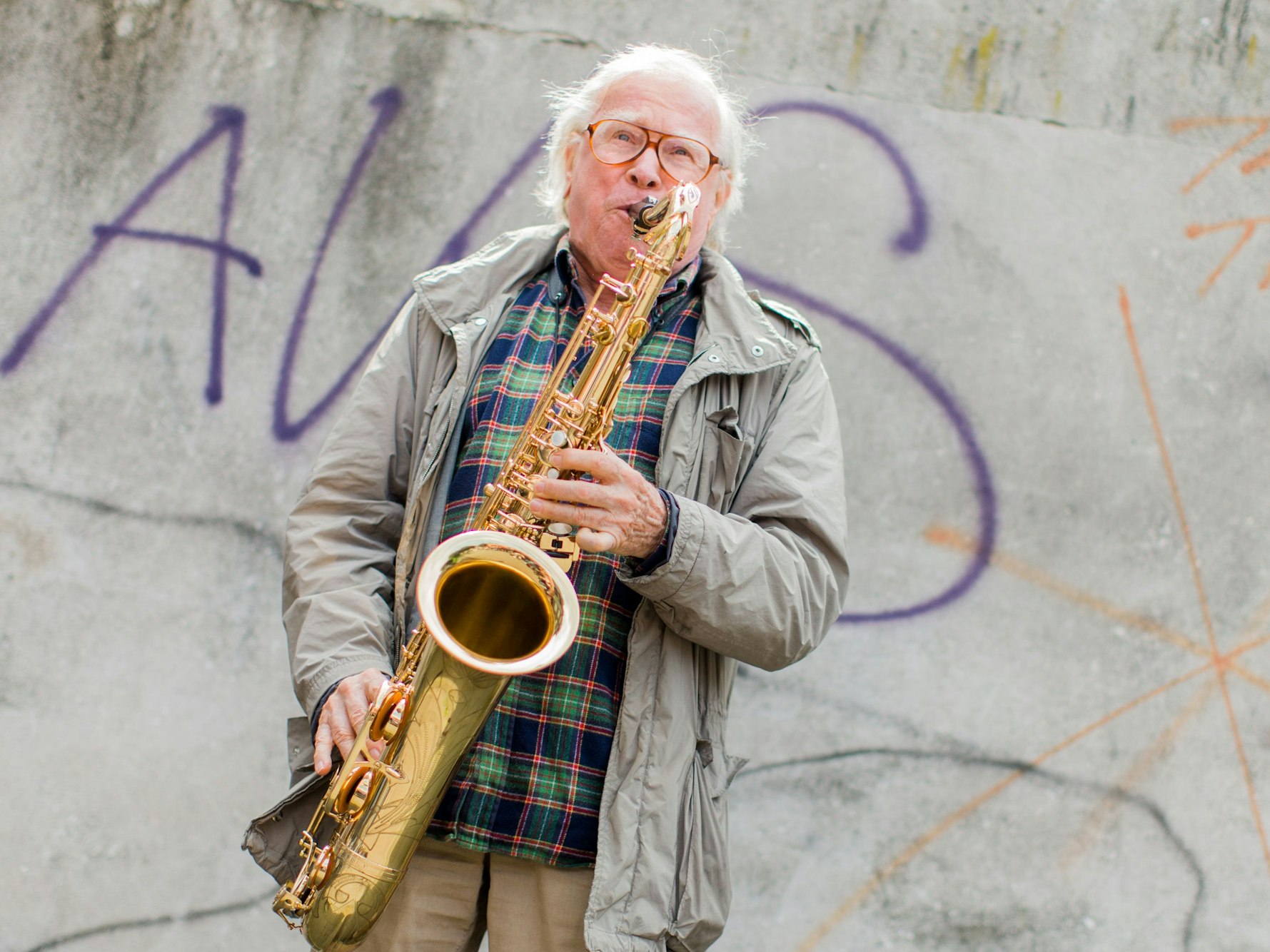 Ein Mann spielt vor einer Wand Saxofon.