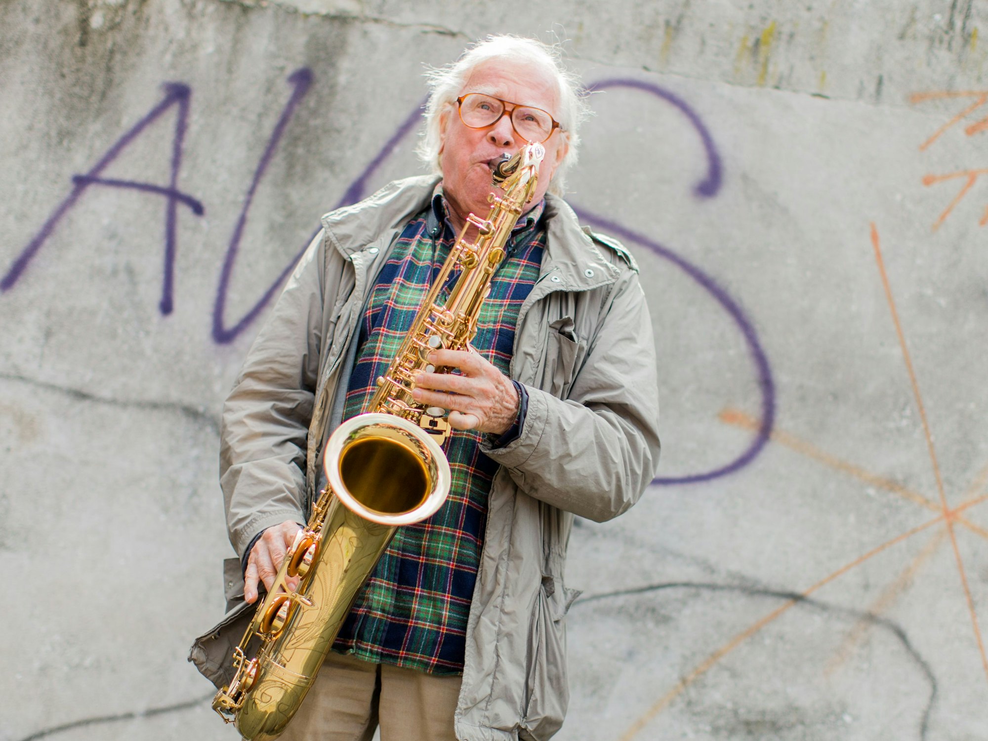 Ein Mann spielt vor einer Wand Saxofon.