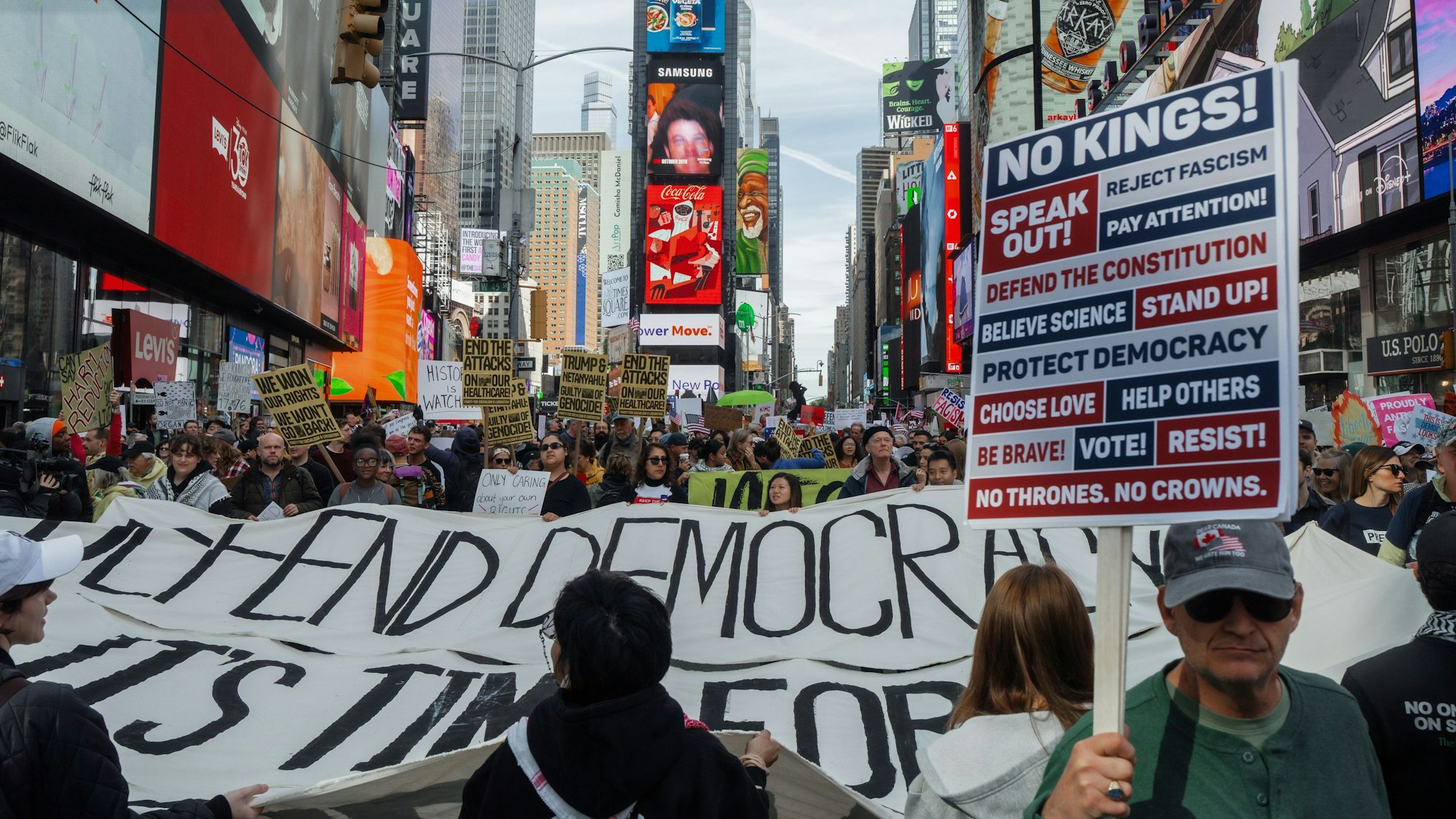Menschen tragen ein Pro-Demokratie-Banner und Plakate während einer Demonstration durch eine Straße, auf der sich unzählige Menschen drängen.