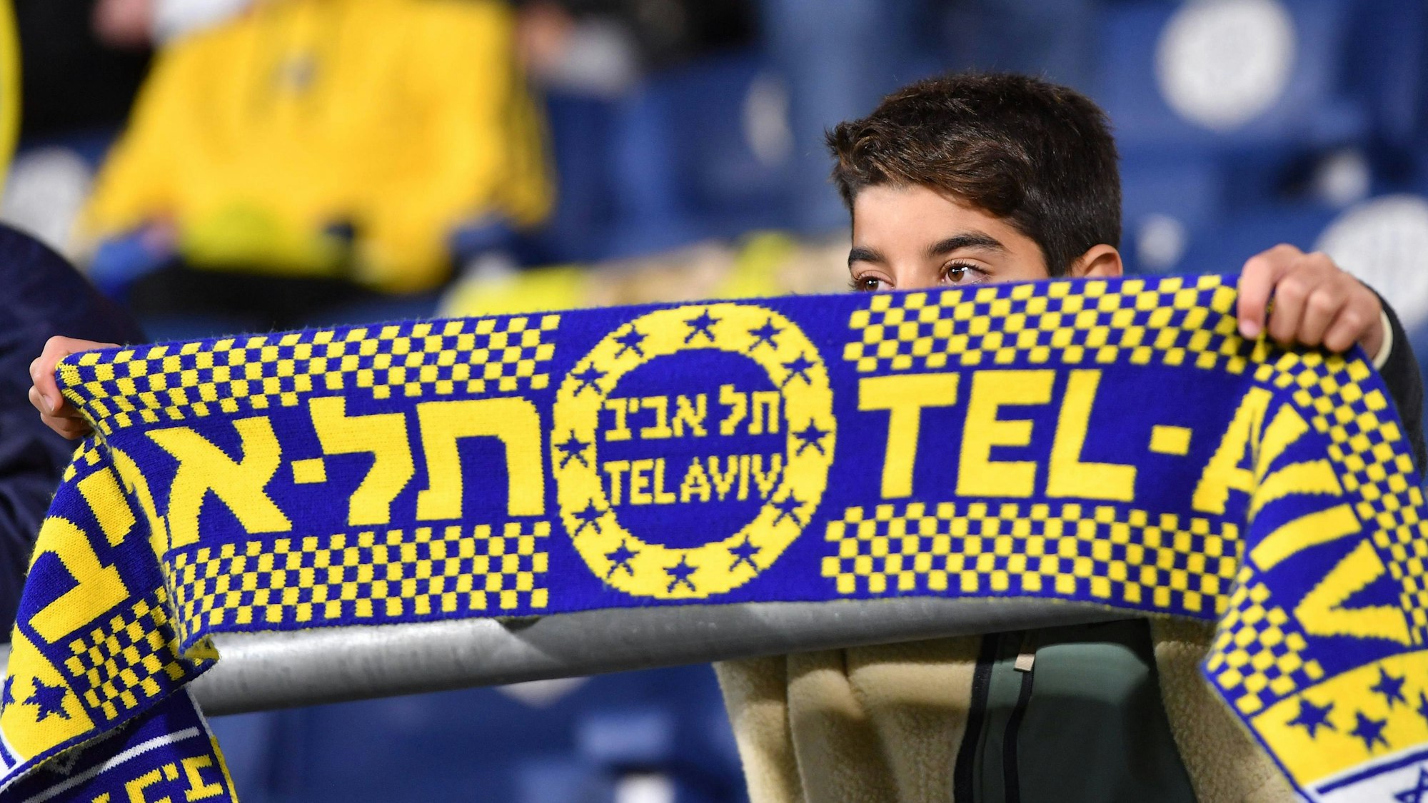 Ein junger Fan hält einen Schal von Maccabi Tel Aviv hoch.