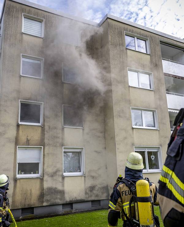 Rauch dringt aus einem Fenster eines Hauses, vor dem drei Feuerwehrleute stehen.