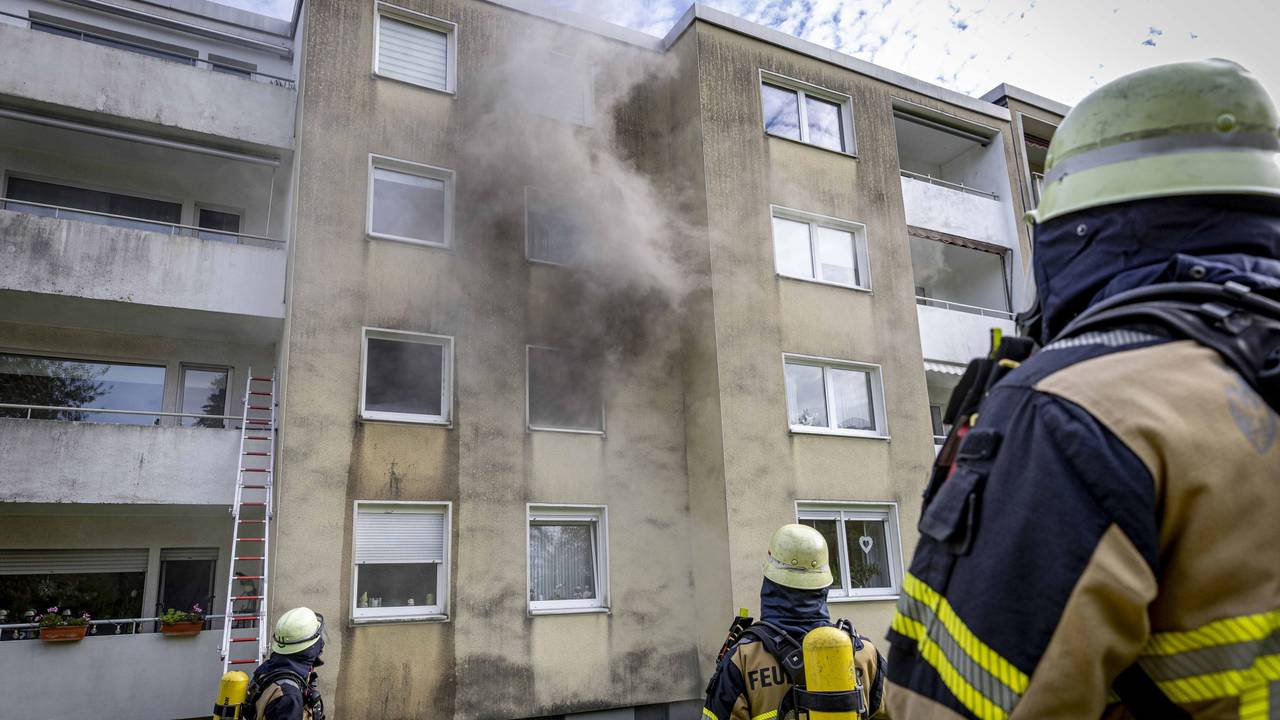 Rauch dringt aus einem Fenster eines Hauses, vor dem drei Feuerwehrleute stehen.