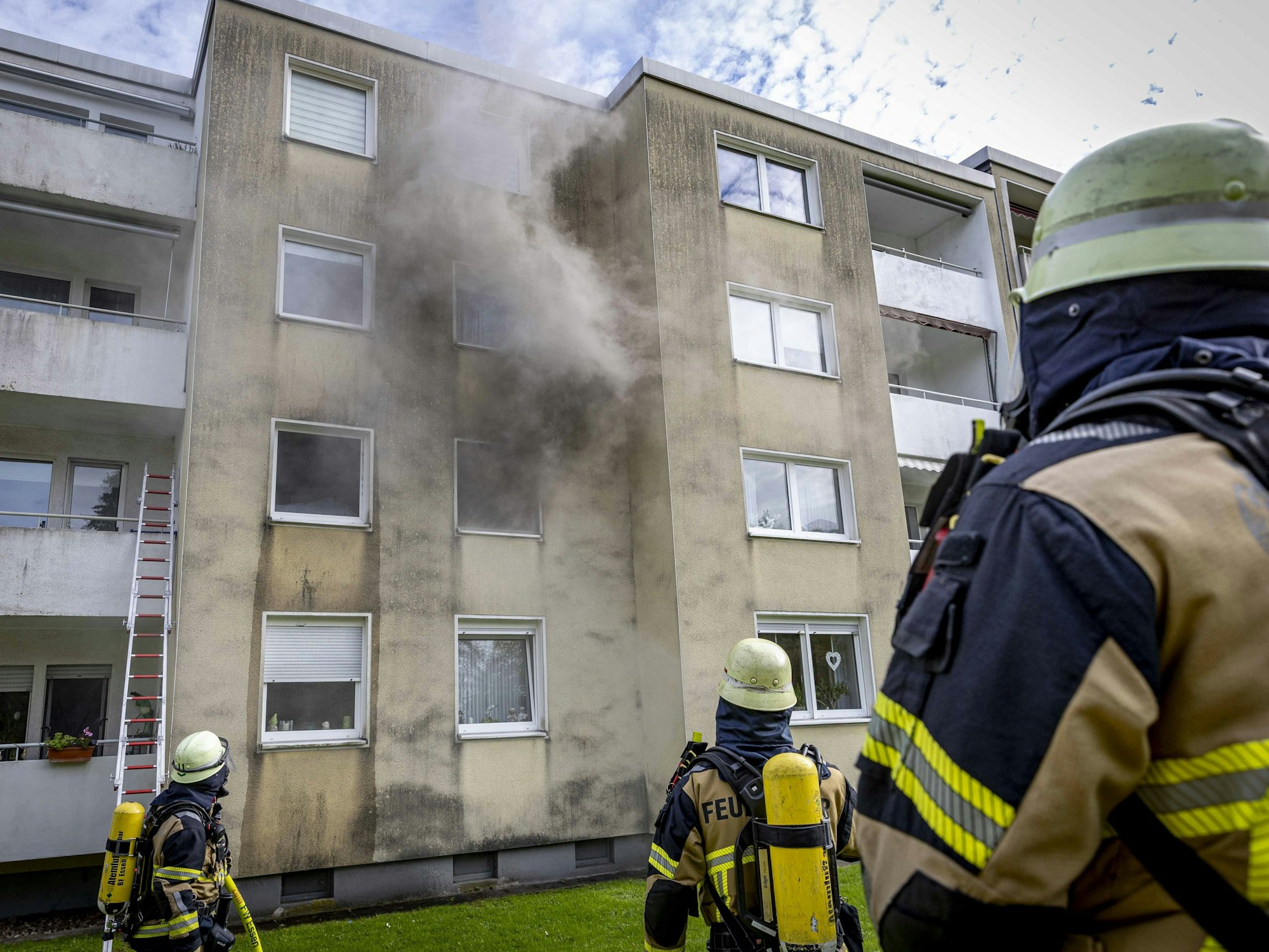 Rauch dringt aus einem Fenster eines Hauses, vor dem drei Feuerwehrleute stehen.