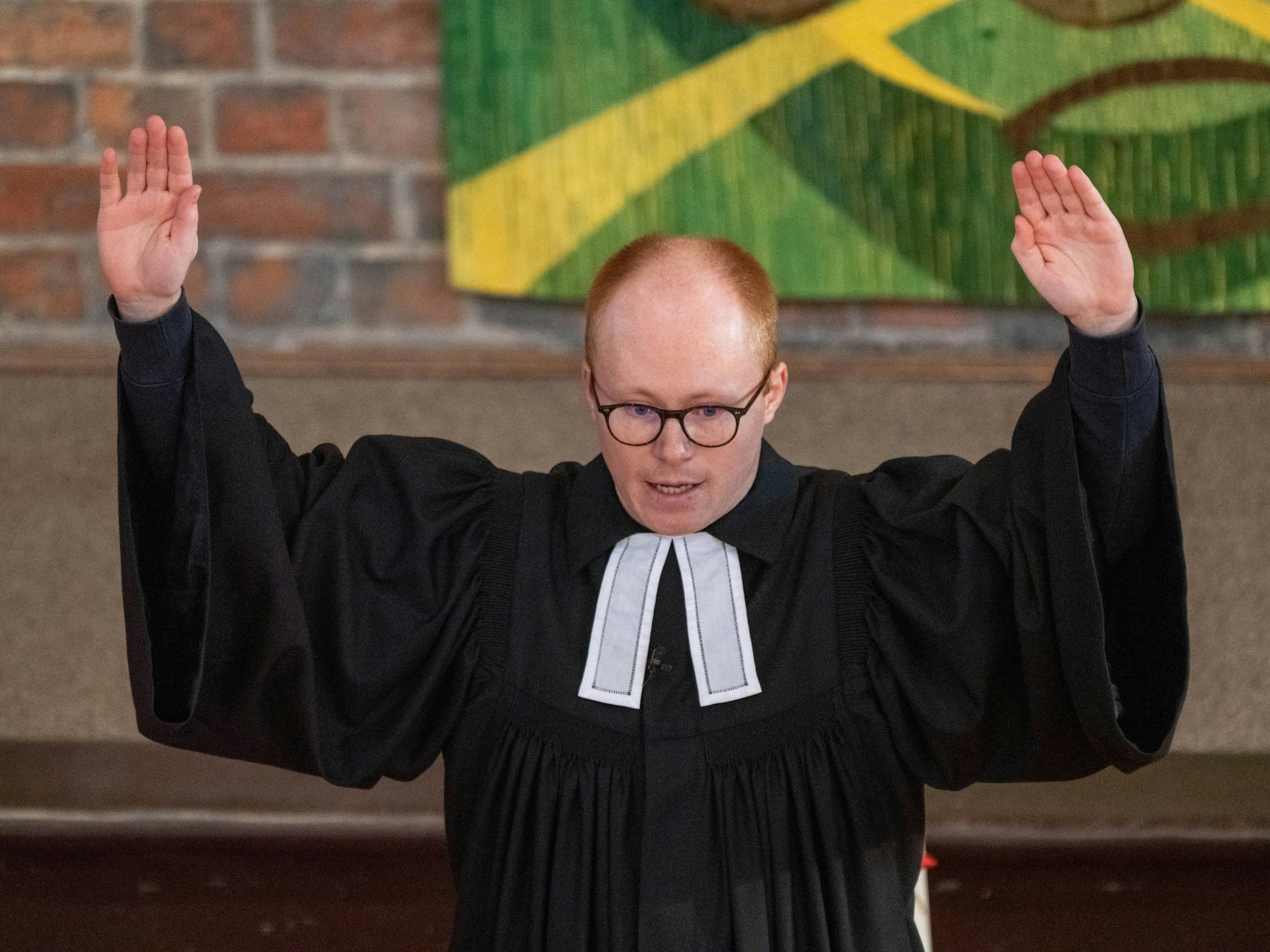 Ein Vikar steht in einer Kirche und hält beide Arme hoch.