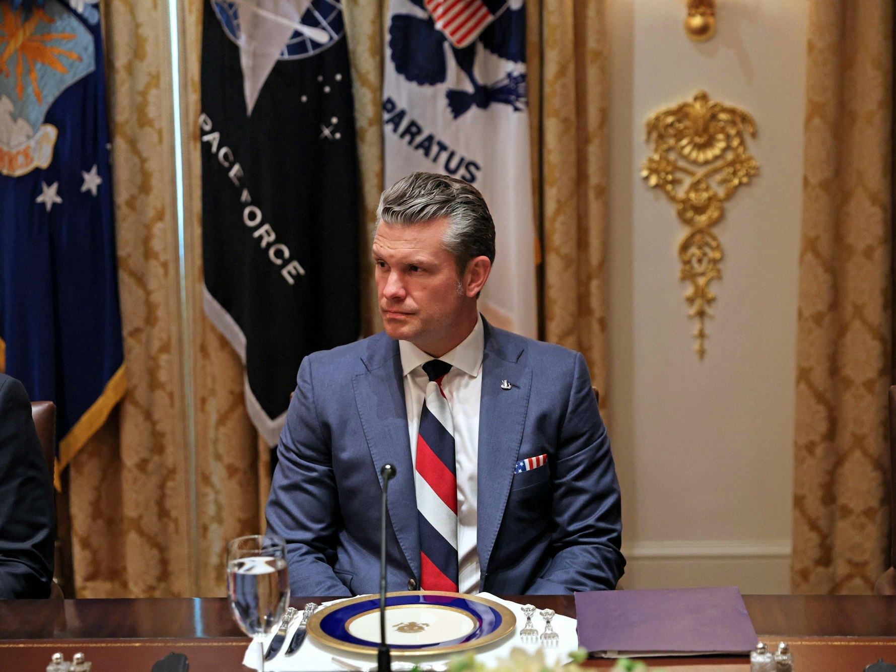 US-Verteidigungsminister Pete Hegseth sitzt an einem gedeckten Tisch und trägt dabei eine weiß, blau und rot gestreifte Krawatte