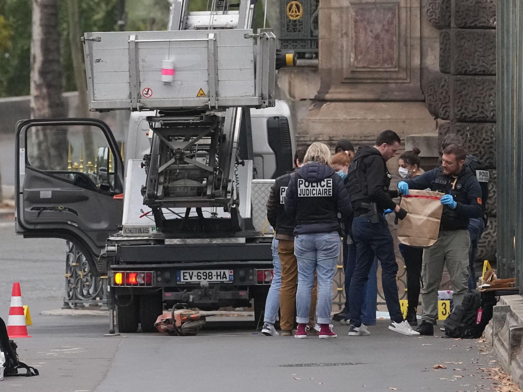 Polizeikräfte stehen an einem Lastenaufzug, einer von ihnen hält eine Tüte in Händen.