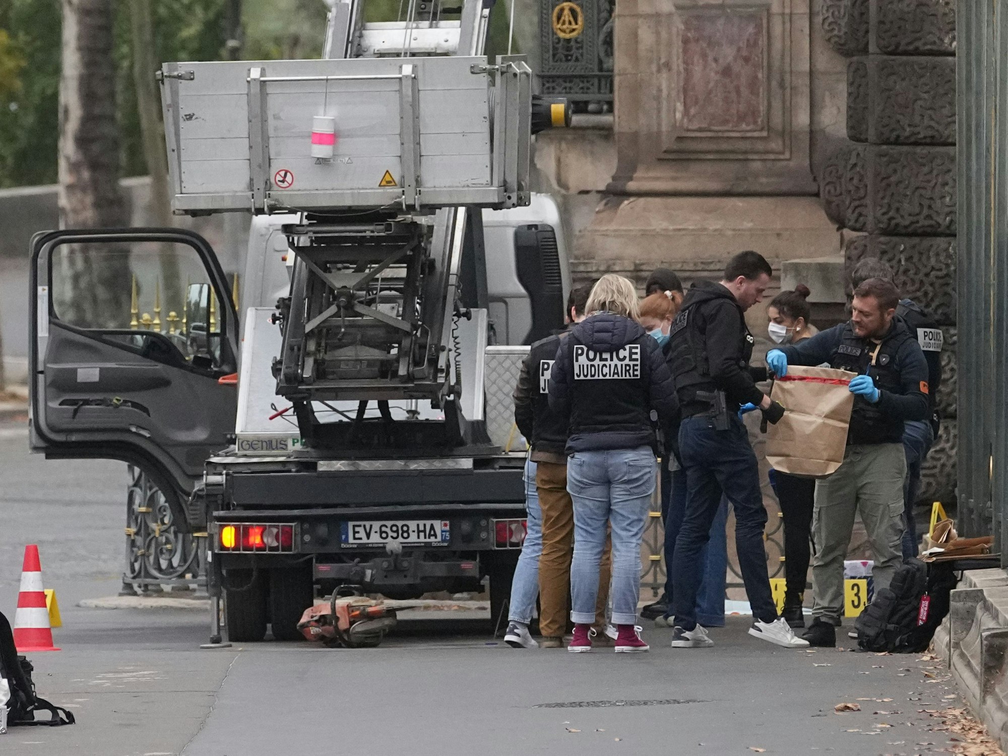 Polizeikräfte stehen an einem Lastenaufzug, einer von ihnen hält eine Tüte in Händen.