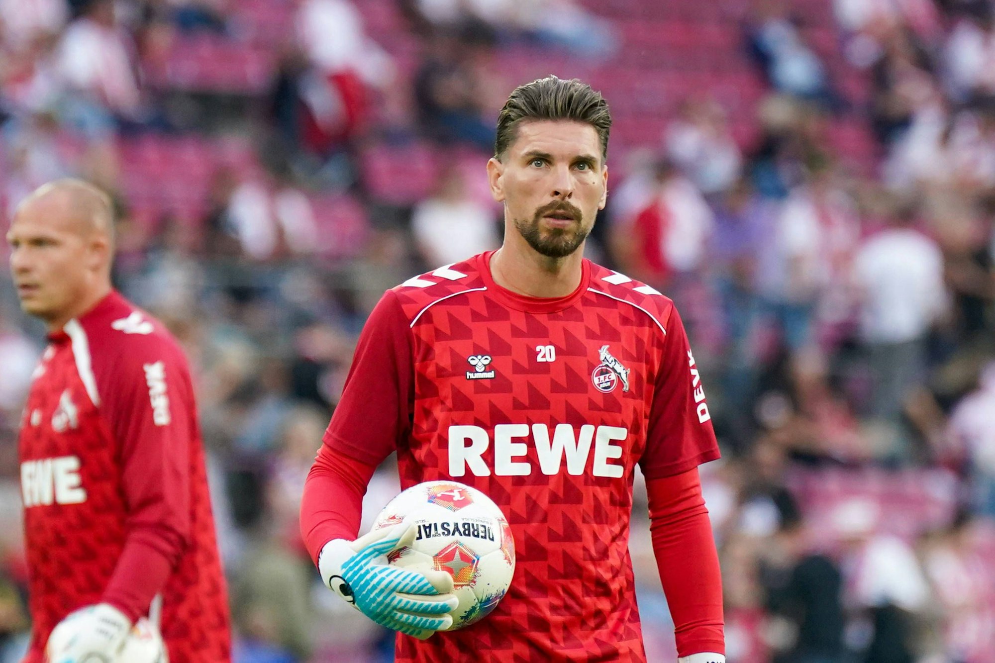 Ron-Robert Zieler hat einen Ball in seiner Hand und guckt in die Ferne.