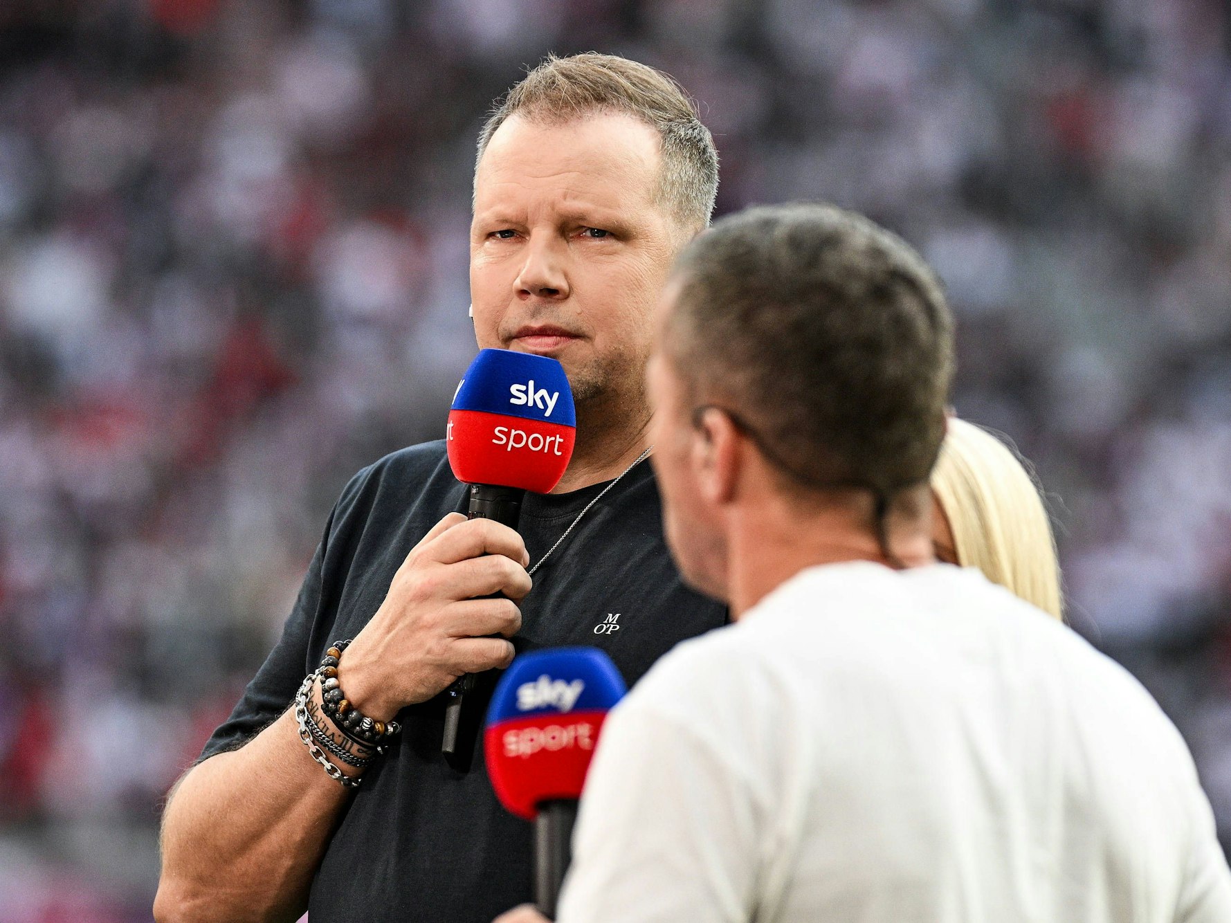 Wolff Fuss hält ein Sky-Mikrofon vor seinen Mund und guckt streng.