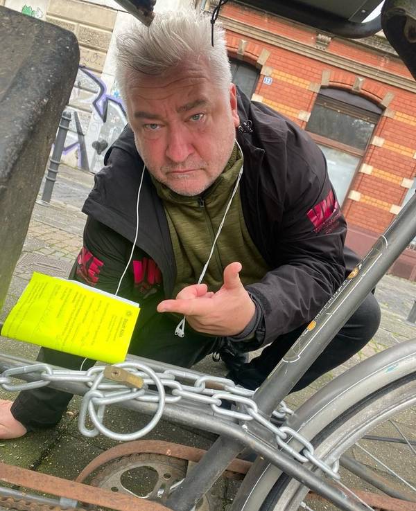 Ein Mann hockt neben einem Fahrrad und zeigt auf einen Zettel, der am Fahrradrahmen befestigt wurde.