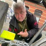 Ein Mann hockt neben einem Fahrrad und zeigt auf einen Zettel, der am Fahrradrahmen befestigt wurde.