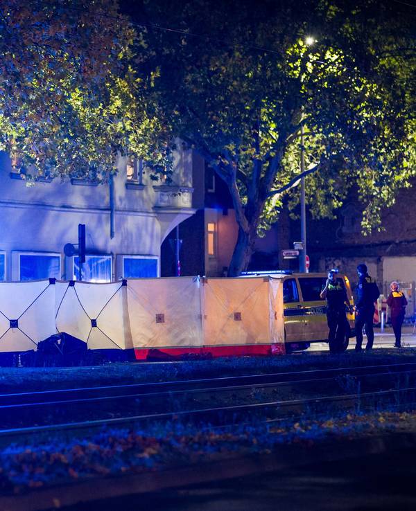 An eine Straße steht ein langer Sichtschutz, dahinter befinden sich mehrere Einsatzkräfte sowie ein Rettungswagen.