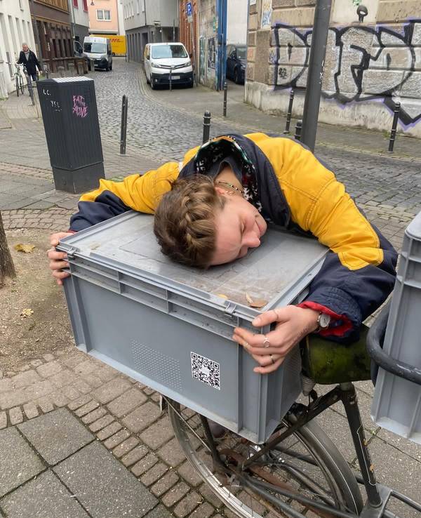 Eine Frau umarmt eine große Kiste, die auf einem Fahrrad steht.