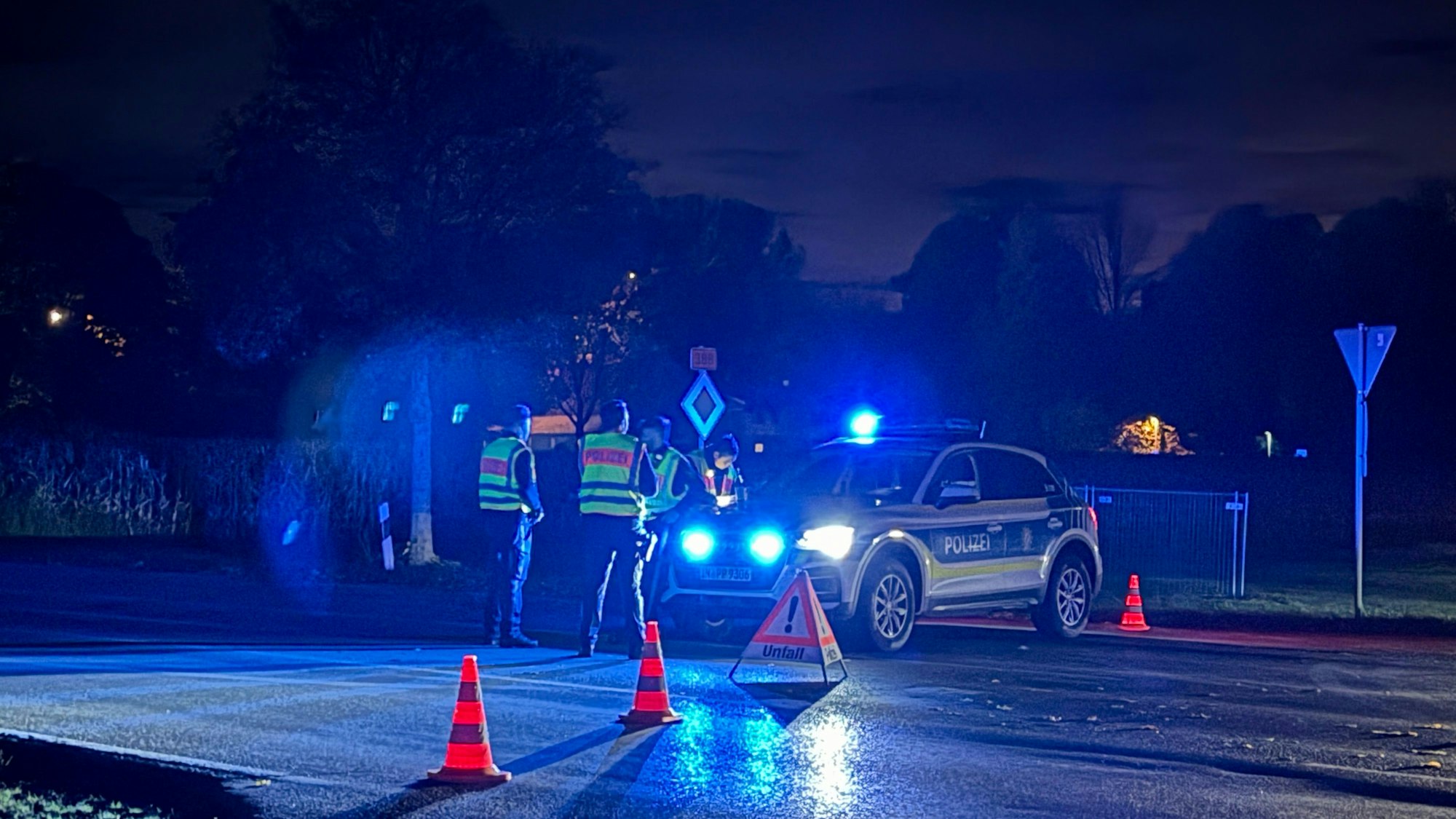 Einsatzkräfte der Polizei stehen an am Mittwochabend (22. Oktober 2025) in Erding an einer abgesperrten Straße.