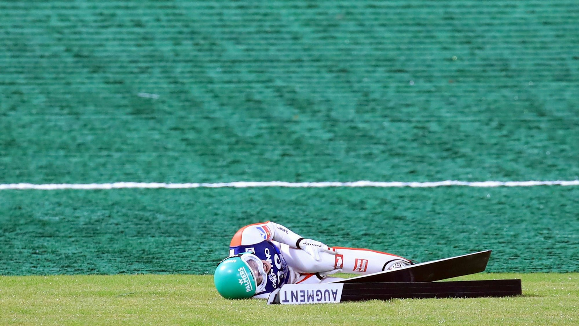 Skispringerin Eva Pinkelnig liegt nach einem Sturz auf dem Gras und hält sich das Knie.