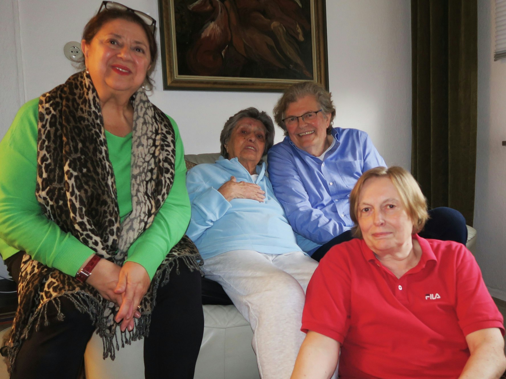 Drei Frauen und ein Mann sitzen auf oder vor einem Sofa.