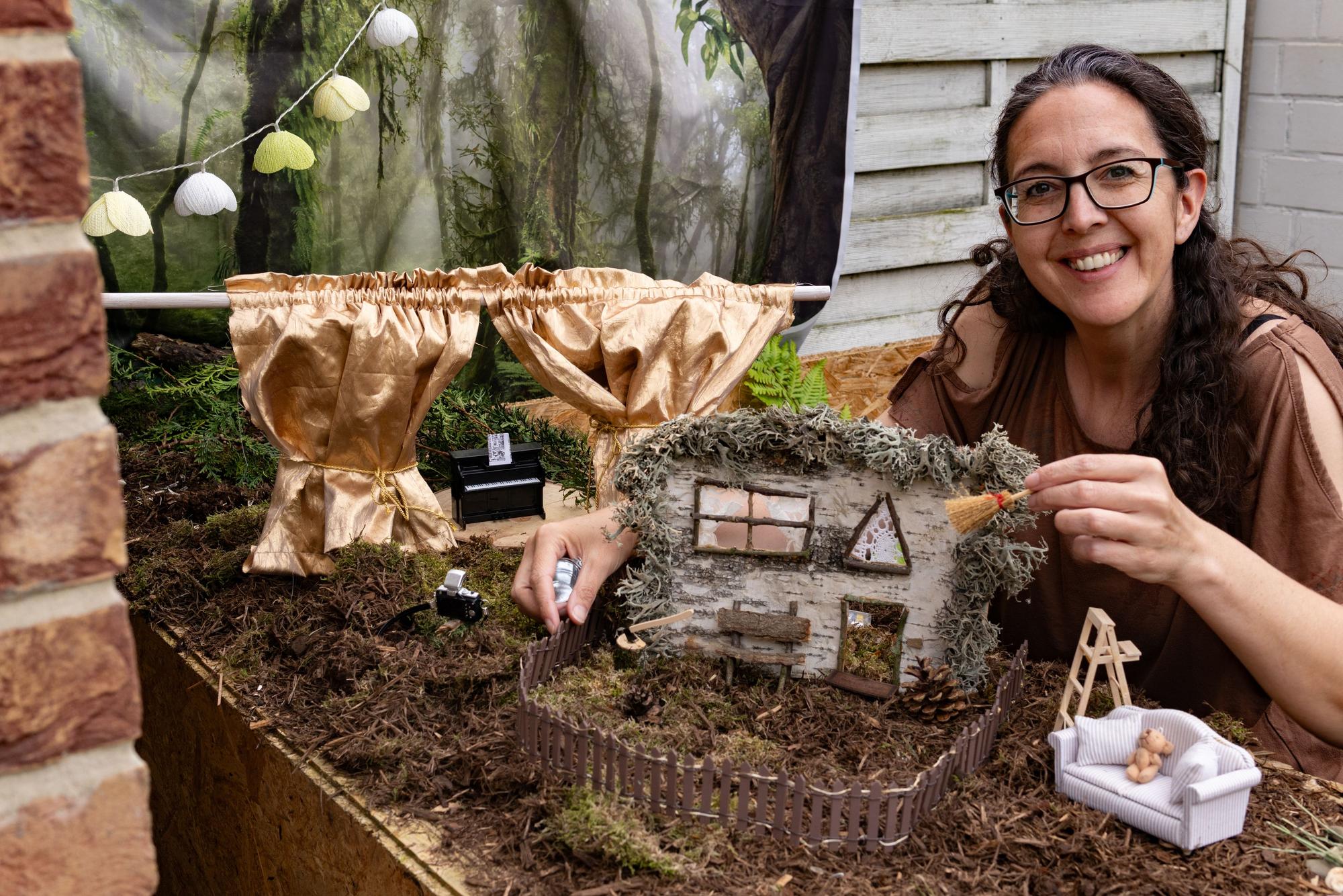 Eine Frau sitzt vor einer Miniatur-Landschaft und lächelt.
