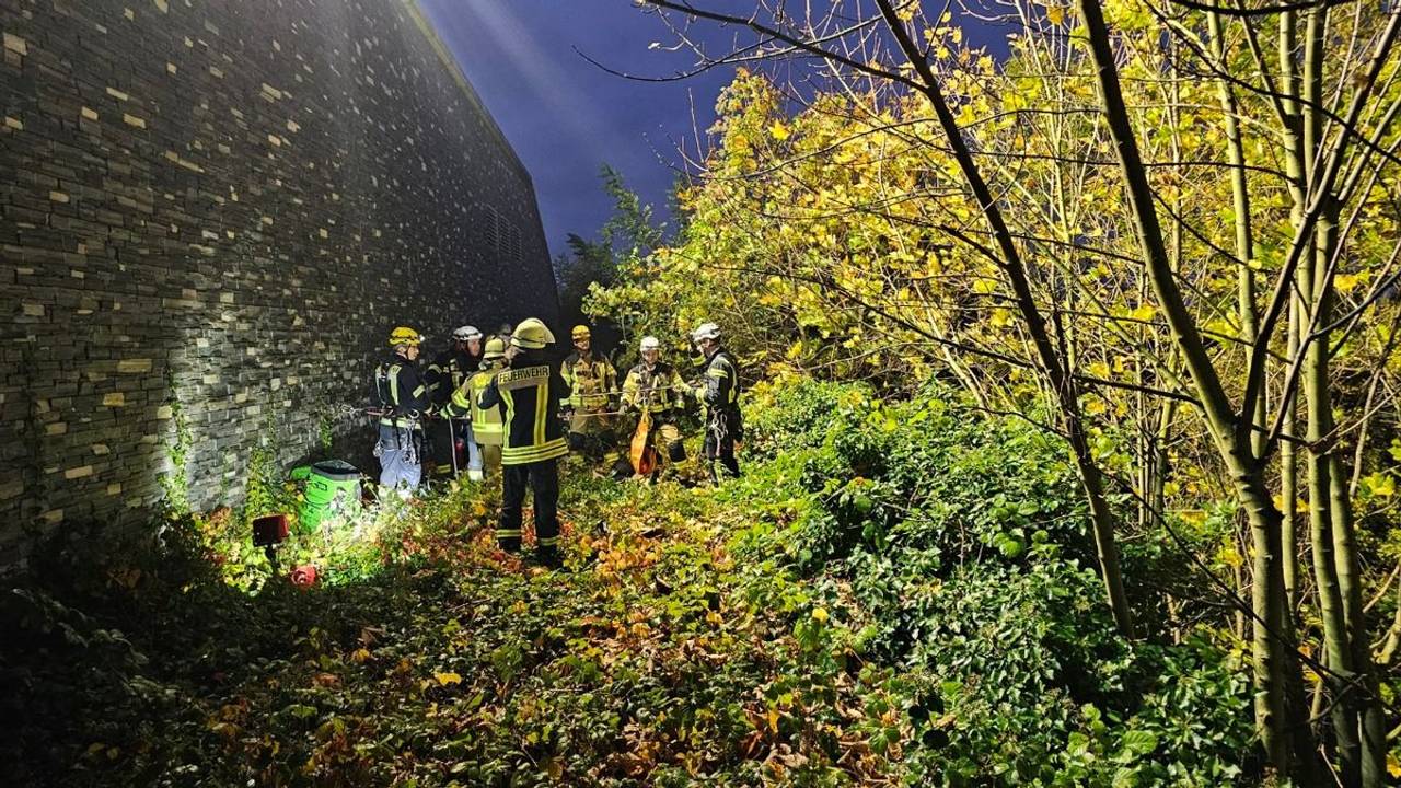 Einsatzkräfte der Feuerwehr stehen unterhalb einer hohen Mauer.
