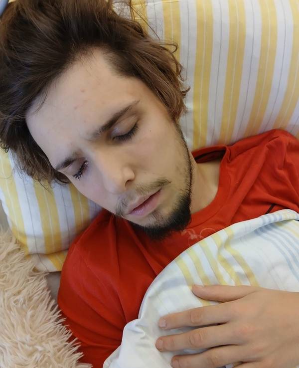 Ein junger Mann liegt mit geschlossenen Augen in einem Krankenhausbett.