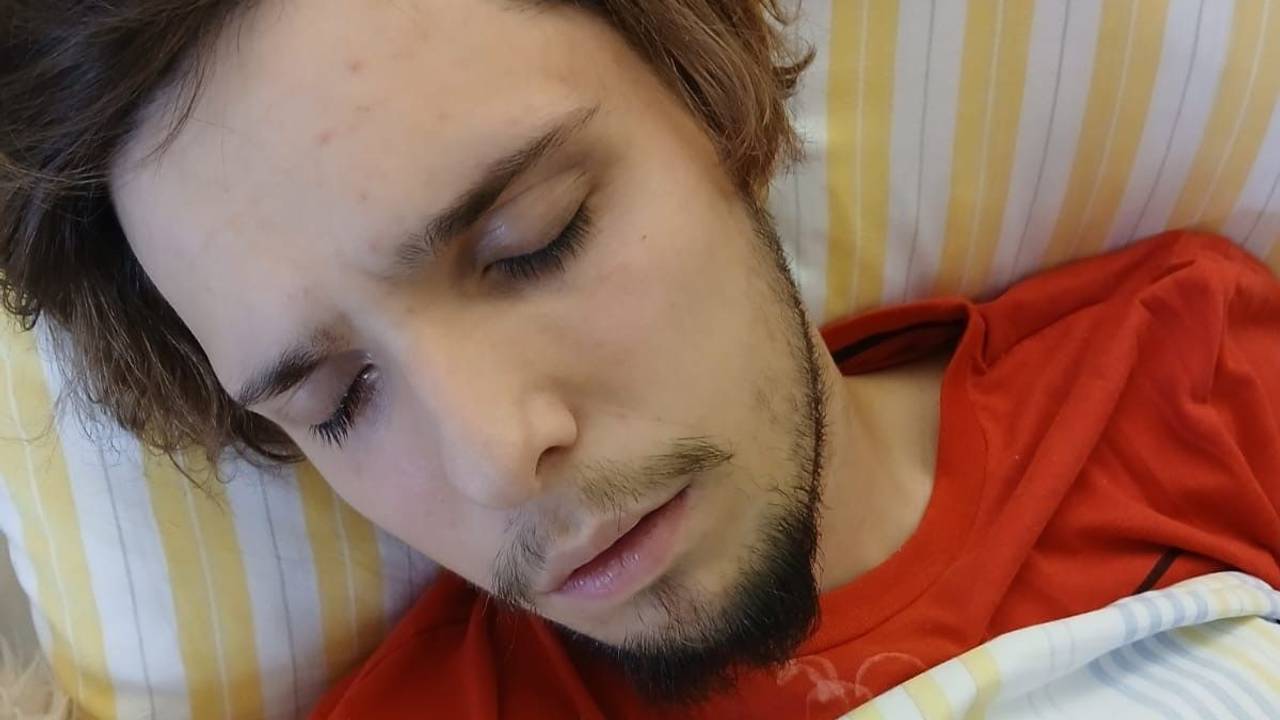 Ein junger Mann liegt mit geschlossenen Augen in einem Krankenhausbett.
