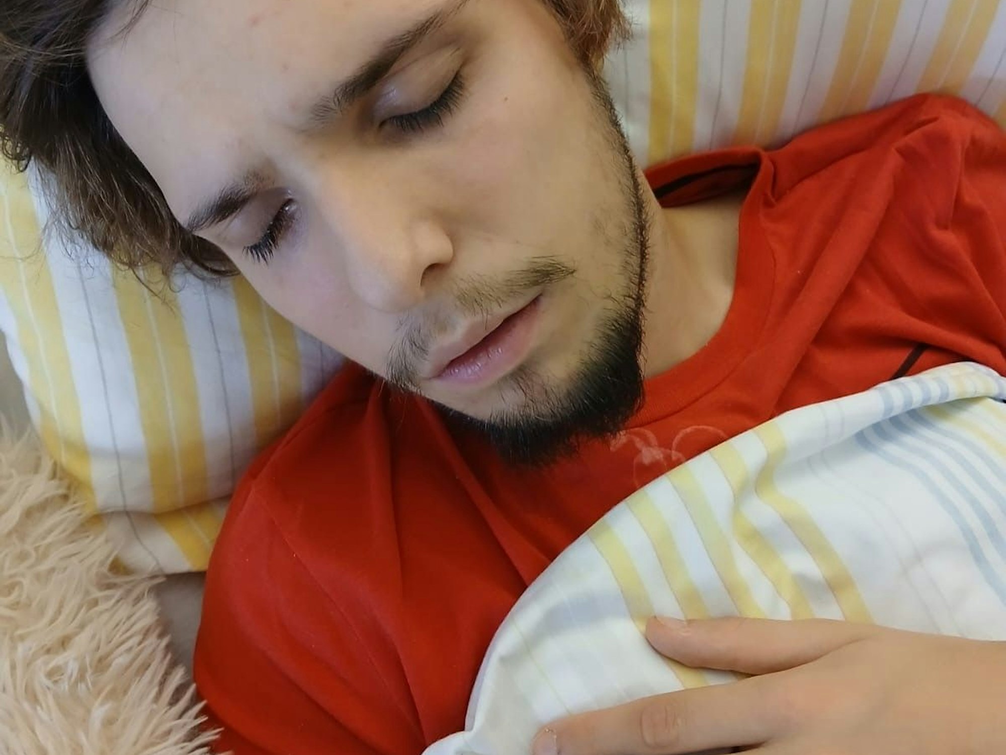 Ein junger Mann liegt mit geschlossenen Augen in einem Krankenhausbett.