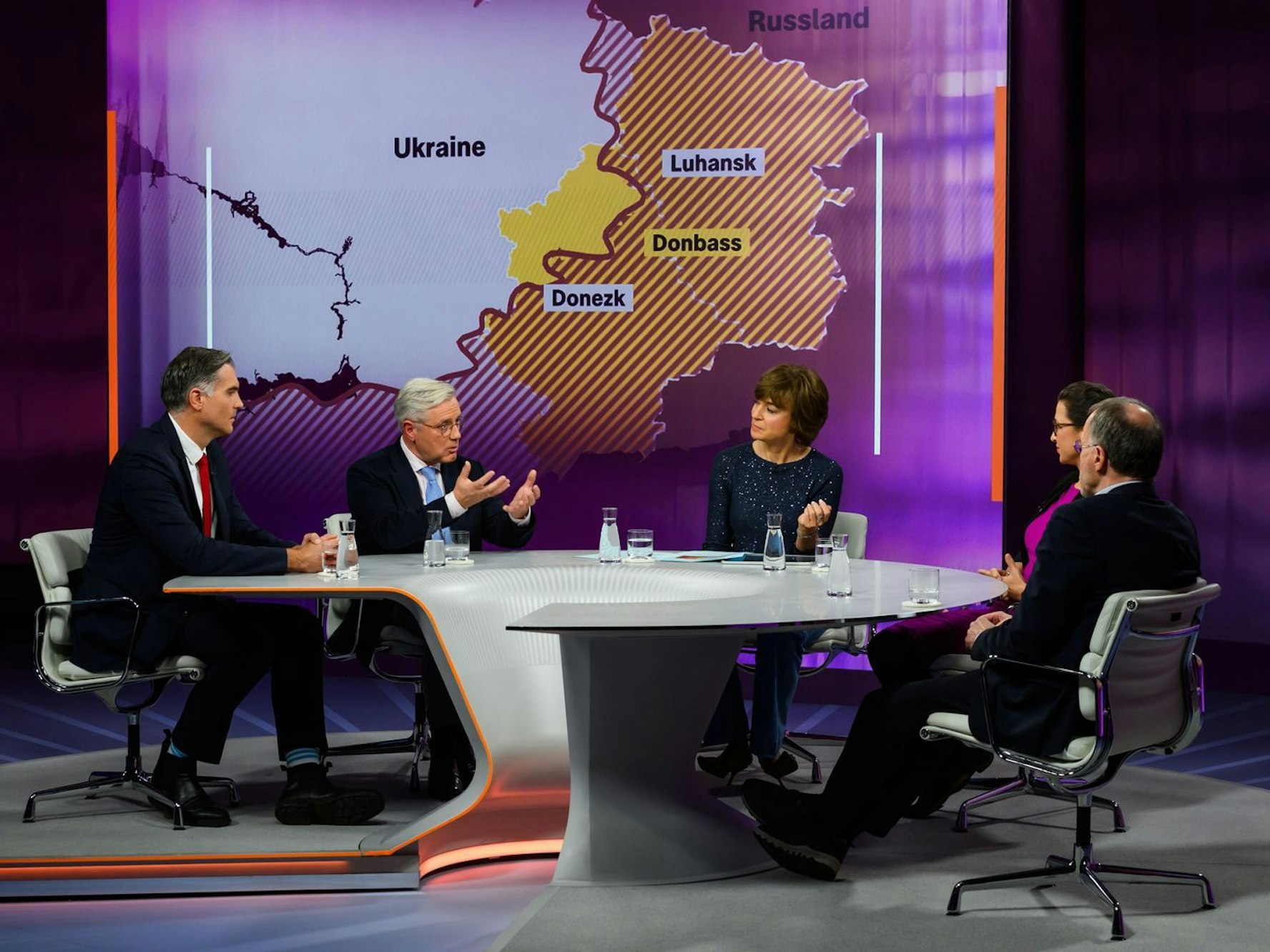 Mehrere Personen sitzen in einem TV-Studio um einen runden Tisch, im Hintergrund eine Karte der Ukraine.