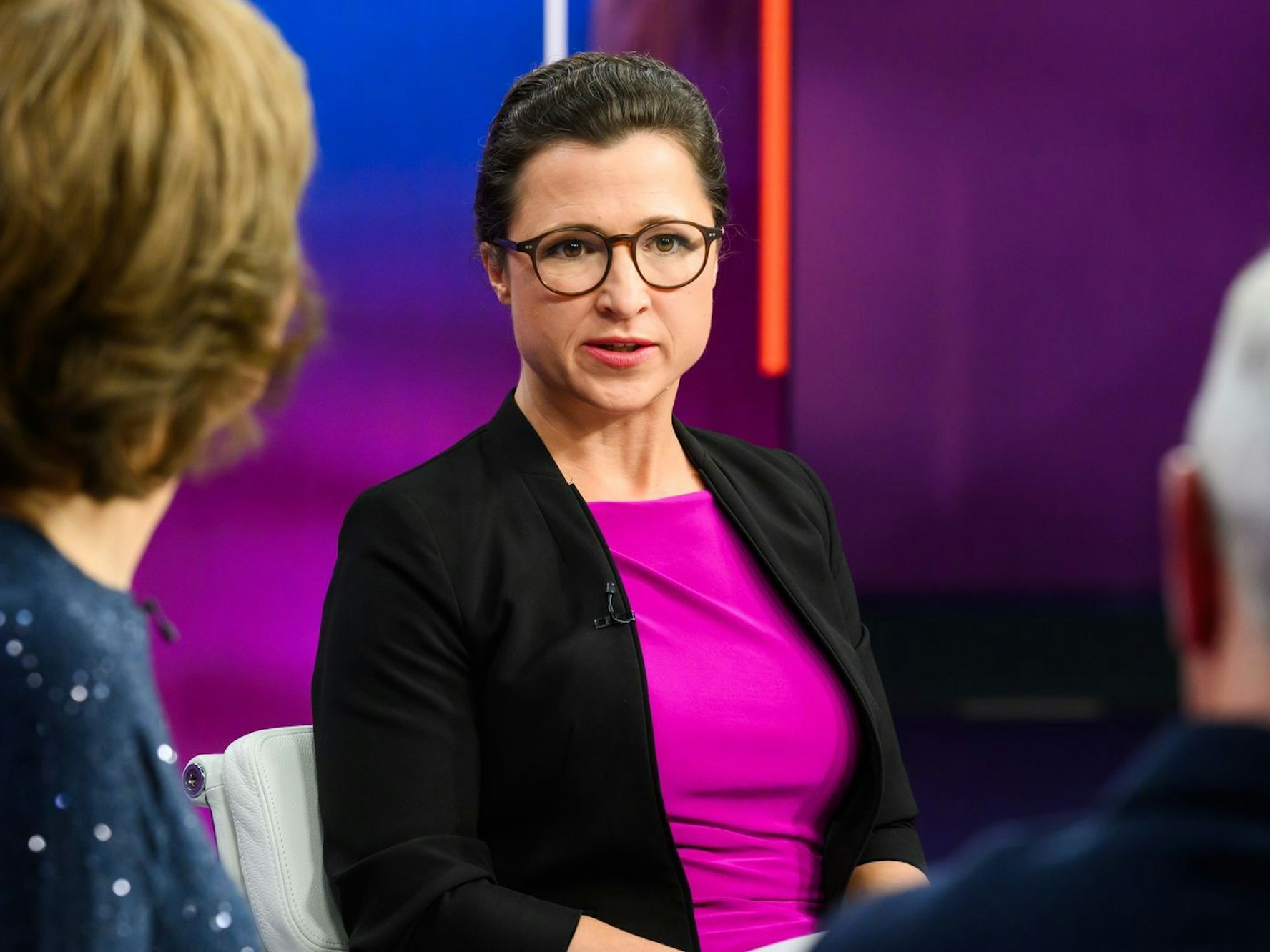 Eine Frau sitzt in einem TV-Studio in der Runde mit anderen.