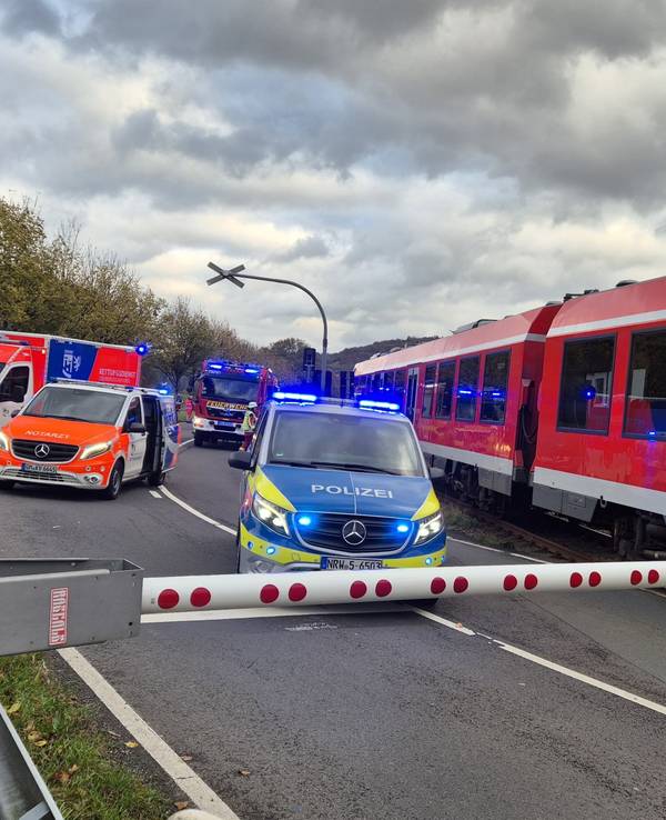 Einsatzfahrzeuge stehen neben einem Zug vor einer geschlossenen Schranke.