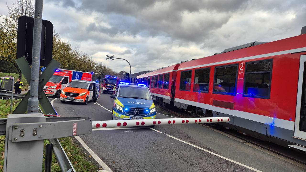 Einsatzfahrzeuge stehen neben einem Zug vor einer geschlossenen Schranke.