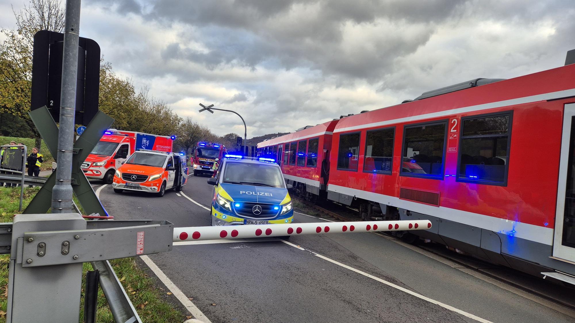 Einsatzfahrzeuge stehen neben einem Zug vor einer geschlossenen Schranke.