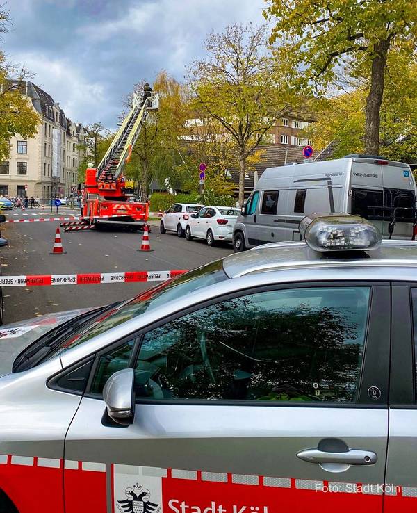 Ein Mann steht im Korb einer Drehleiter, die an einen Straßenbaum heranreicht. Die Straße ist mit Flatterband abgesperrt.