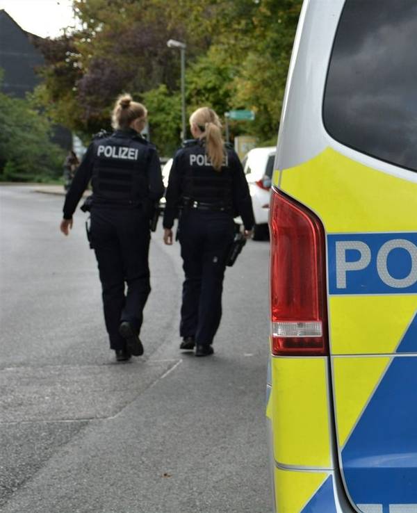 Zwei Polizistinnen laufen an einem Polizeifahrzeug entlang.
