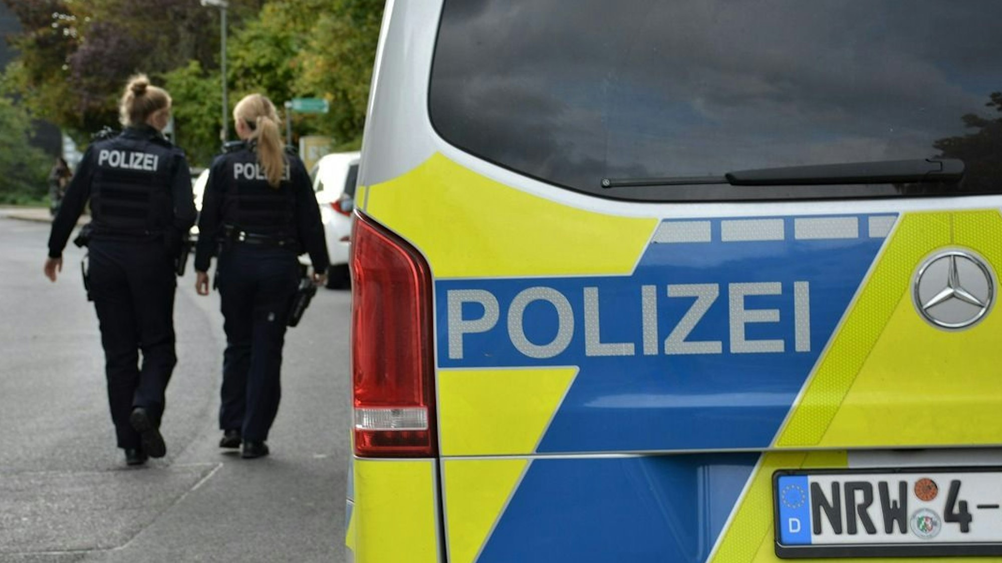 Zwei Polizistinnen laufen an einem Polizeifahrzeug entlang.