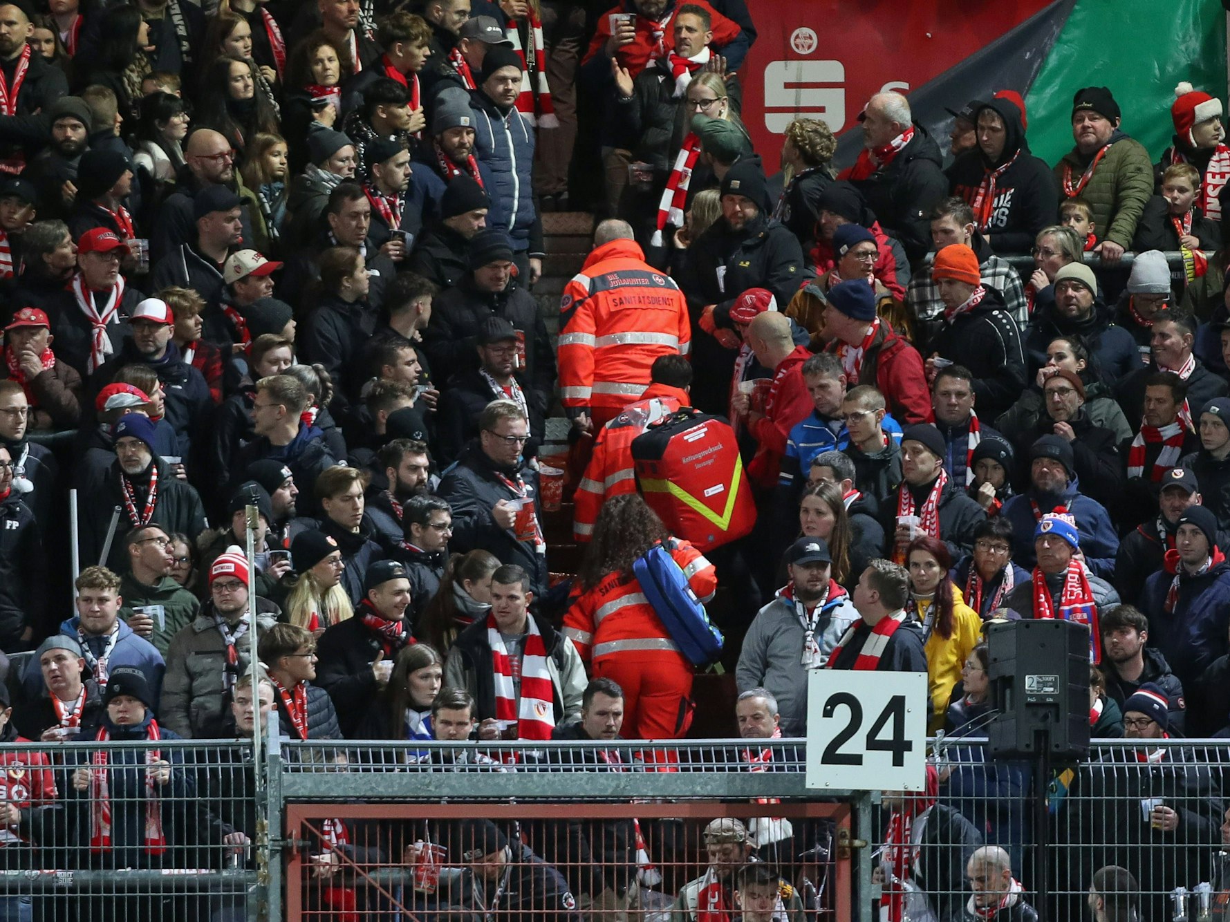 Sanitäter gehen auf einer Tribüne voller Fans eine Treppe nach oben.