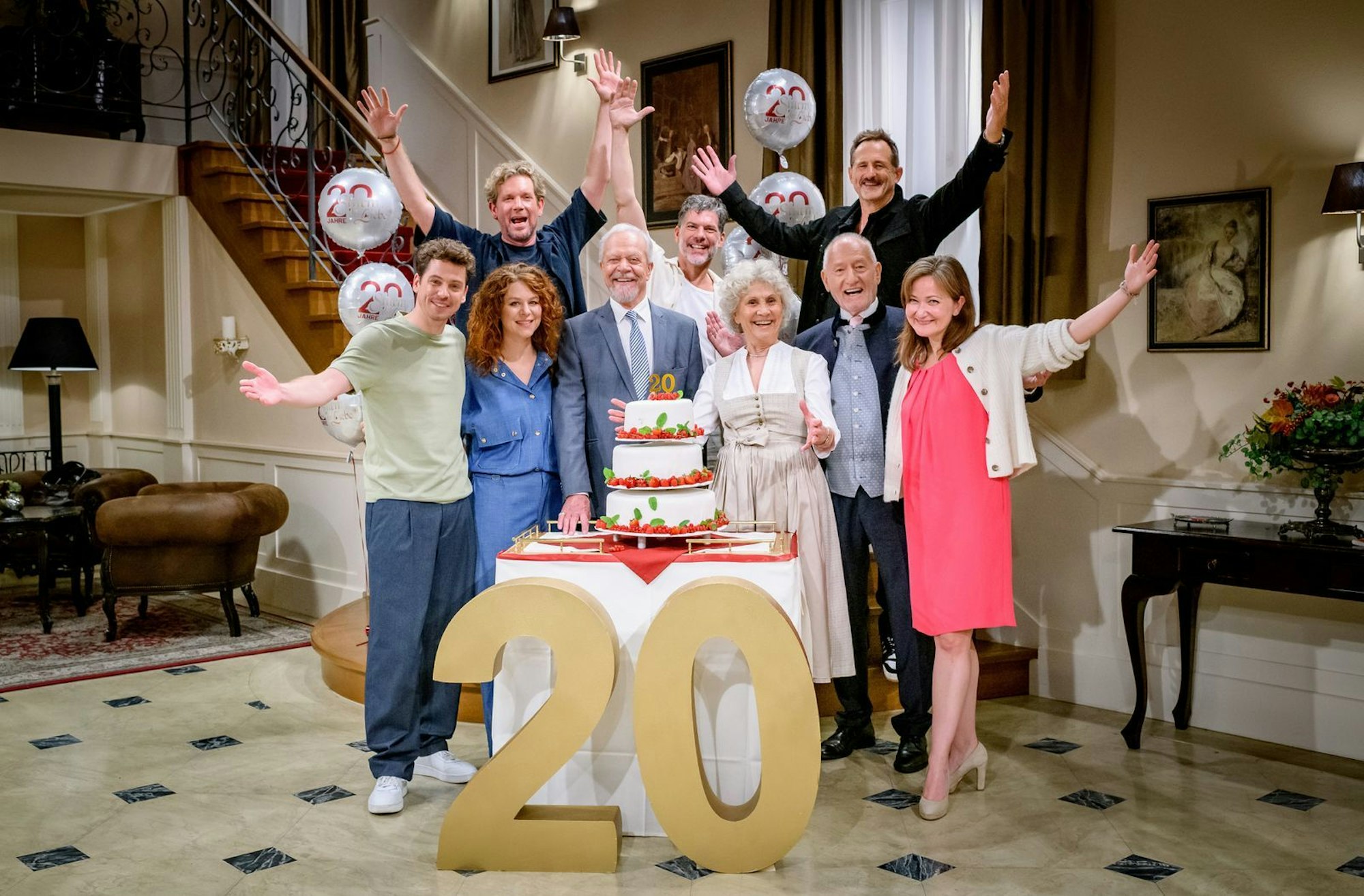 Seit zwei Jahrzehnten begeistert die ARD-Telenovela „Sturm der Liebe“ ihr Publikum. Anlässlich des Jubiläums wurde am Set gefeiert. Unter den Gästen befanden sich Produzent Peter Proske-Clayton (hinten links), Gregory B. Waldis sowie Marcus Ammon (hinten rechts), Geschäftsführer Content bei Bavaria Fiction. In der ersten Reihe freuten sich, von links: Anthony Paul, Johanna Graen, Dirk Galuba, Antje Hagen, Sepp Schauer und Lara Okamoto (Redakteurin BR) gemeinsam über das Jubiläum. (Bild: ARD / Christof Arnold )