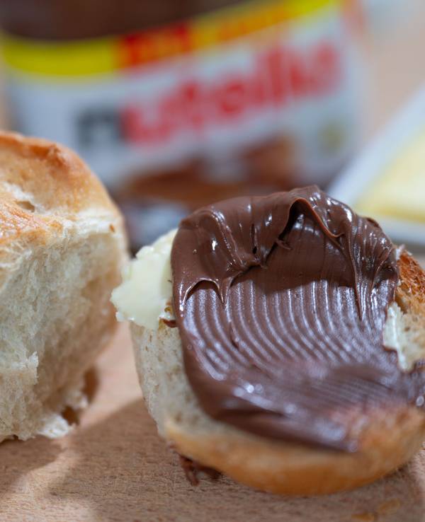 Ein Brötchen mit Nutella liegt auf einem Frühstücksbrett.