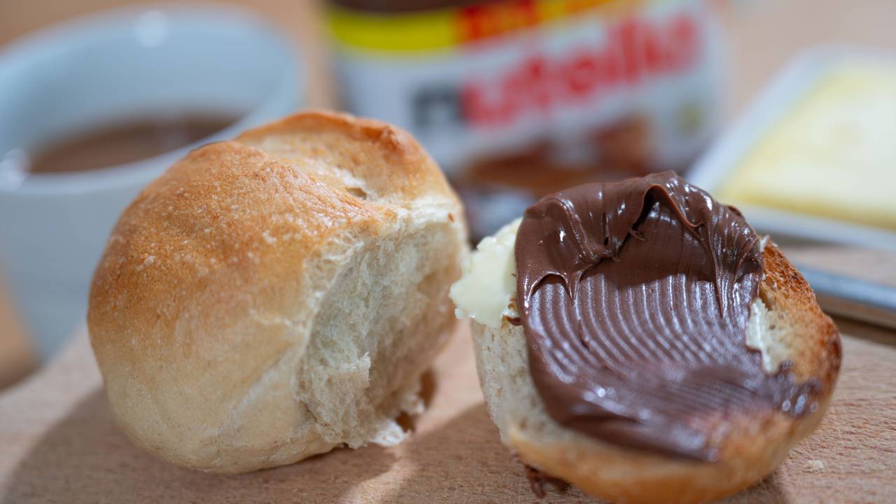 Ein Brötchen mit Nutella liegt auf einem Frühstücksbrett.