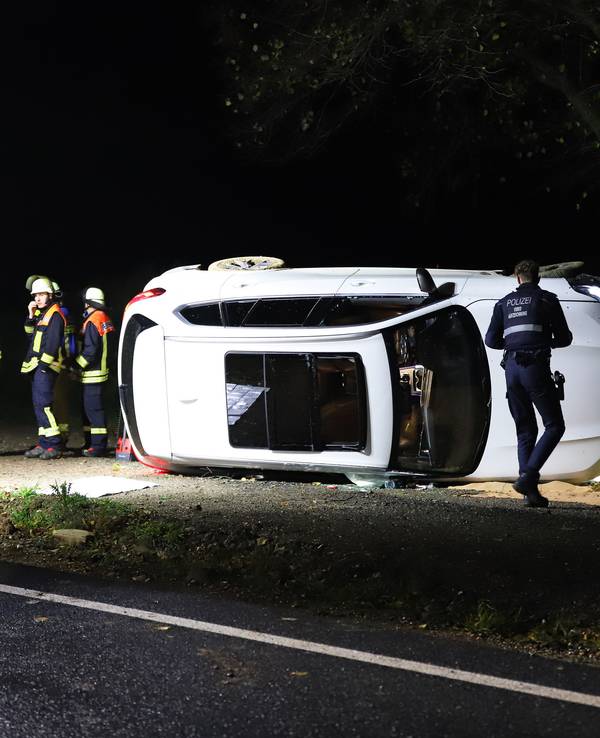 Einsatzkräfte von Polizei und Feuerwehr stehen an einem Pkw, der auf der Seite liegt.