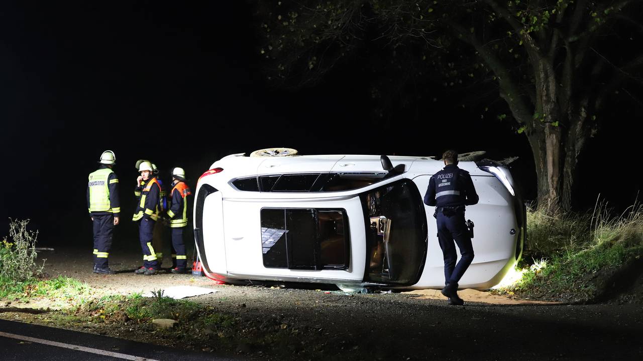 Einsatzkräfte von Polizei und Feuerwehr stehen an einem Pkw, der auf der Seite liegt.