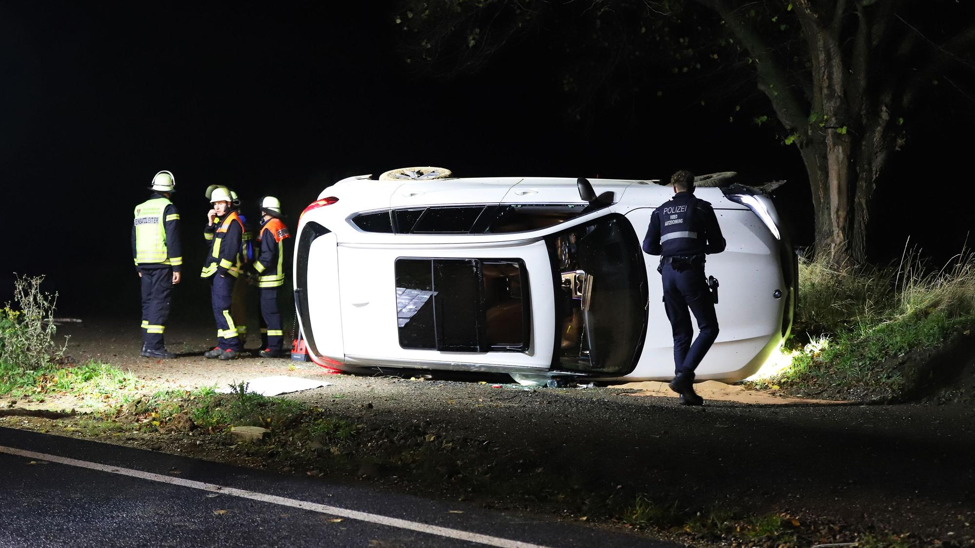 Einsatzkräfte von Polizei und Feuerwehr stehen an einem Pkw, der auf der Seite liegt.