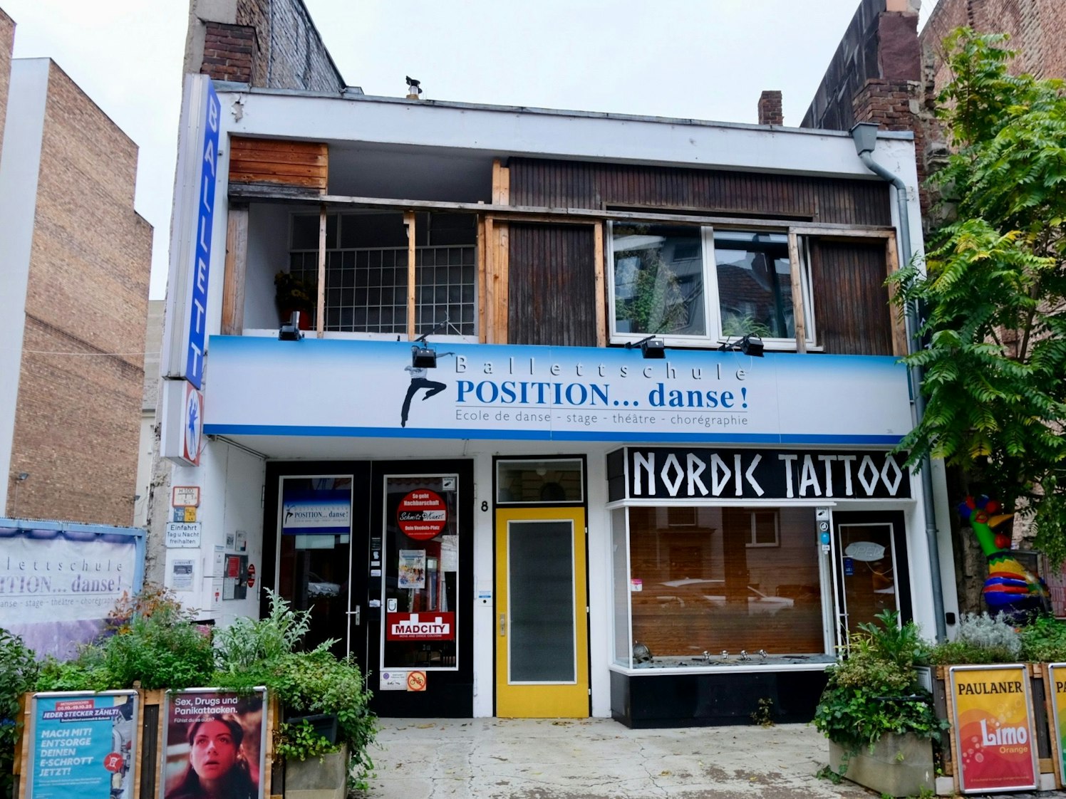 Ein zweigeschossiges würfelartiges Gebäude steht zwischen zwei Backsteingebäuden.