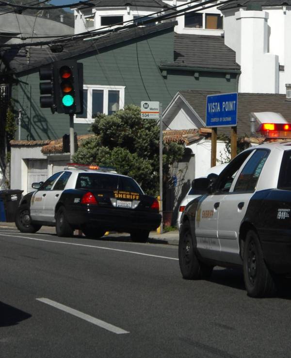 Zwei „Los Angeles County Sheriff“ Autos auf einer Straße mit Häusern im Hintergrund