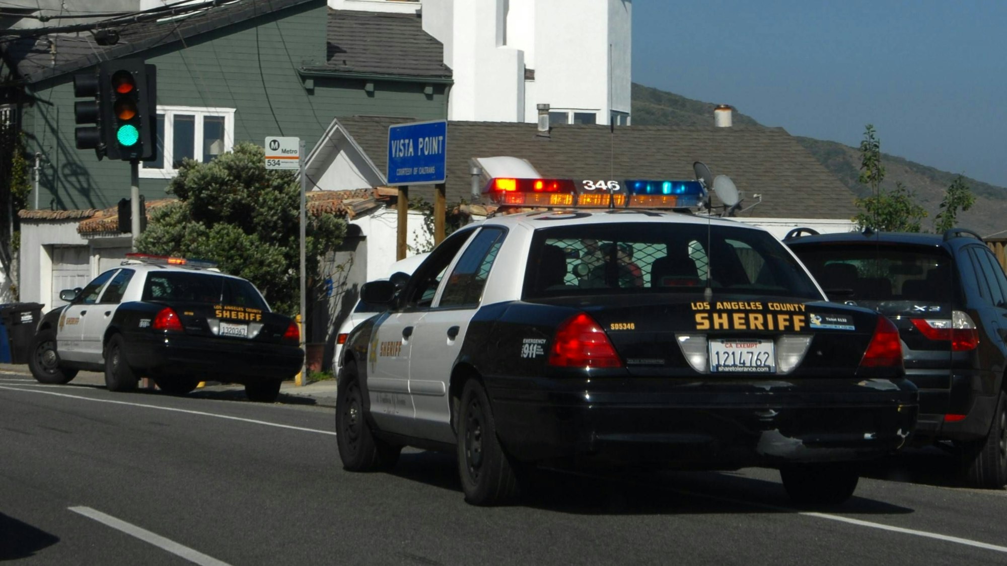 Zwei „Los Angeles County Sheriff“ Autos auf einer Straße mit Häusern im Hintergrund
