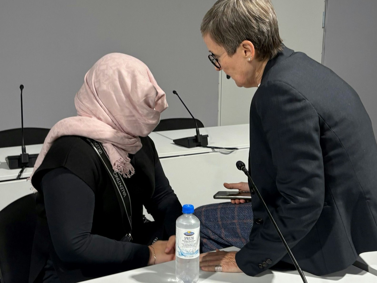 Die Angeklagte hat einen Schal um ihren Kopf und ihr Gesicht gebunden, um nicht erkennbar zu sein. Sie unterhält sich im Gerichtssaal mit ihrer Anwältin.