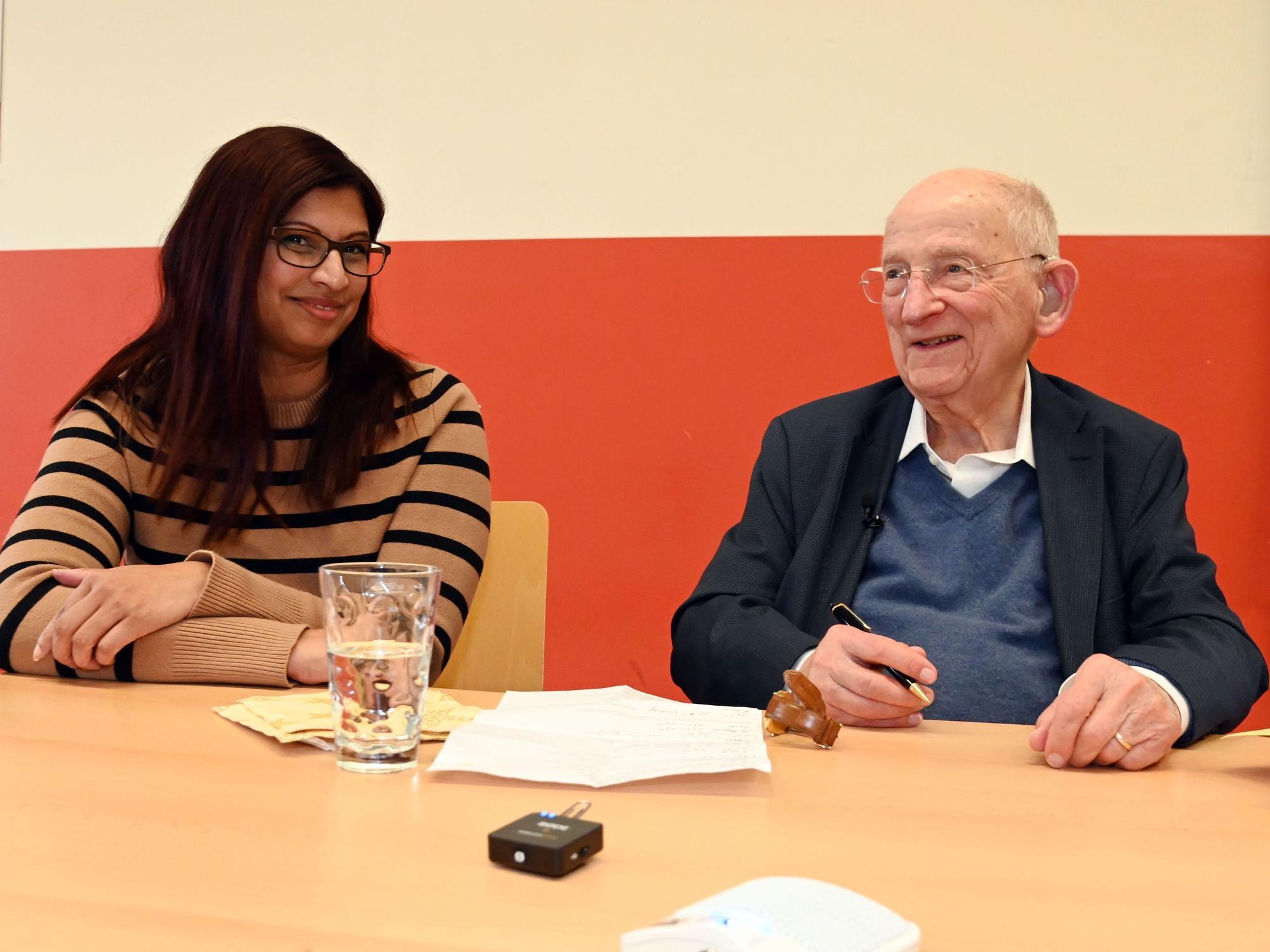 Ein alter Herr und eine junge Frau sitzen am Tisch und unterhalten sich.