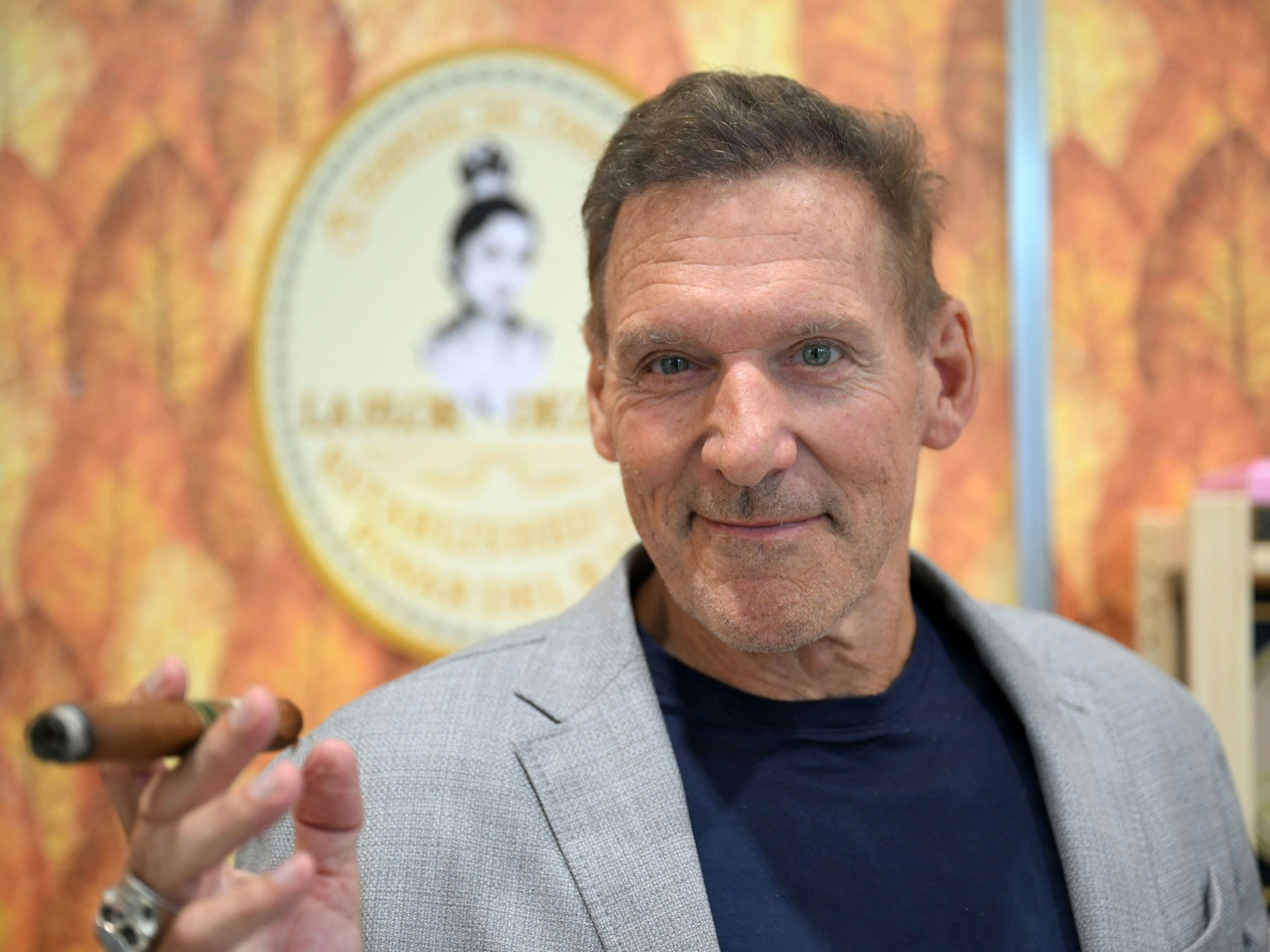 Der Schauspieler Ralf Moeller steht bei der Messe Intertabac am Messestand eines Zigarrenfabrikanten und pafft eine Zigarre.